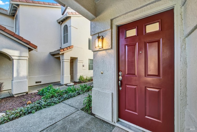 view of exterior entry with stucco siding and a tile roof