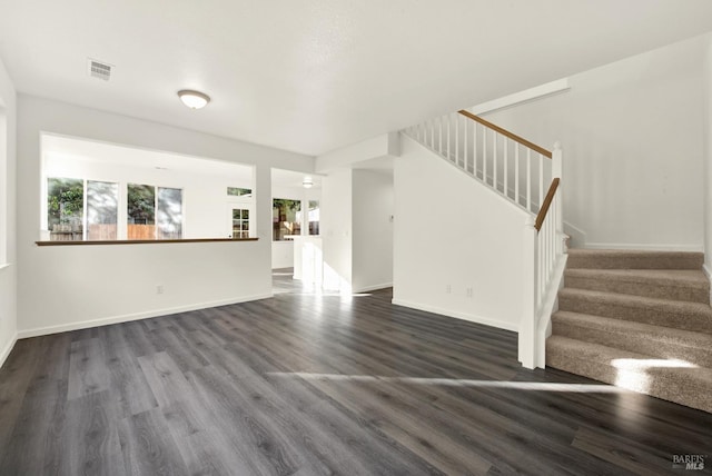 unfurnished living room featuring dark wood-type flooring, baseboards, visible vents, and stairway