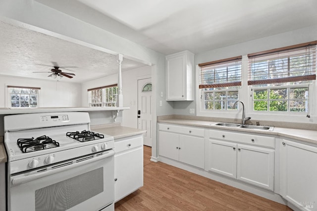 kitchen featuring sink, white range with gas stovetop, light hardwood / wood-style flooring, ceiling fan, and white cabinets