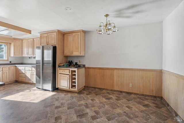 kitchen with light brown cabinets, stainless steel fridge, decorative light fixtures, a notable chandelier, and wooden walls