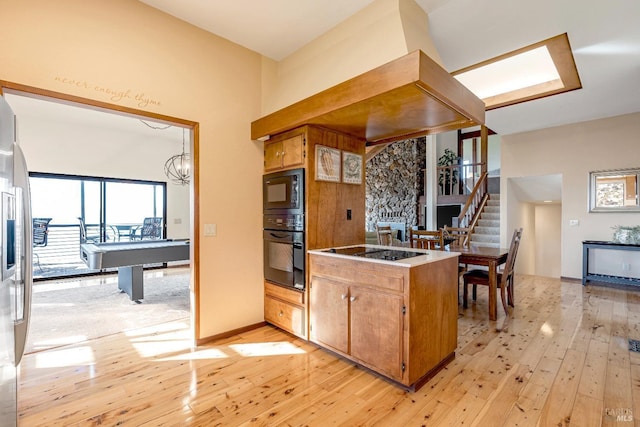 kitchen with black appliances, a chandelier, brown cabinetry, and light wood-style floors