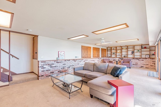 living room featuring a ceiling fan, light carpet, stairway, and brick wall