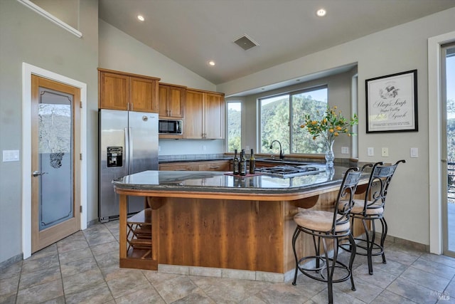 kitchen with kitchen peninsula, stainless steel fridge, a breakfast bar, black microwave, and lofted ceiling