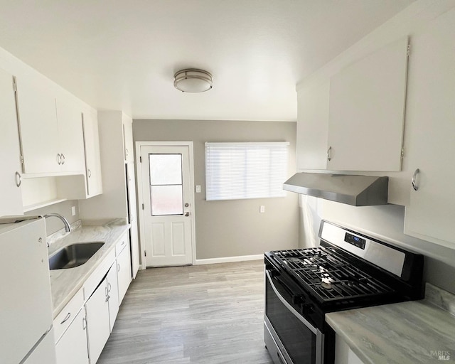 kitchen featuring white fridge, white cabinets, sink, stainless steel range with gas stovetop, and wall chimney exhaust hood