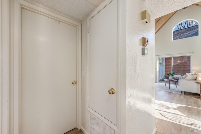 hallway featuring wood-type flooring, a textured ceiling, and lofted ceiling