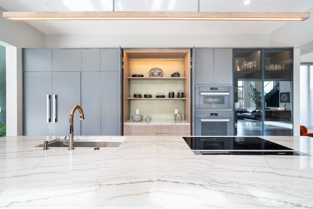 kitchen featuring double oven, sink, light stone counters, gray cabinets, and black electric cooktop