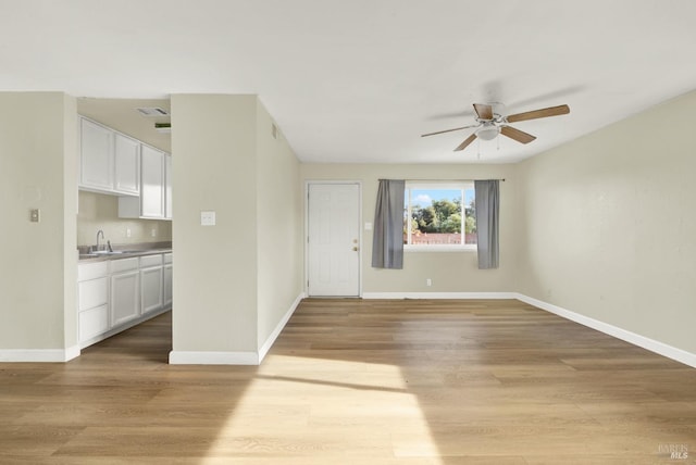 unfurnished living room with sink, ceiling fan, and light hardwood / wood-style flooring