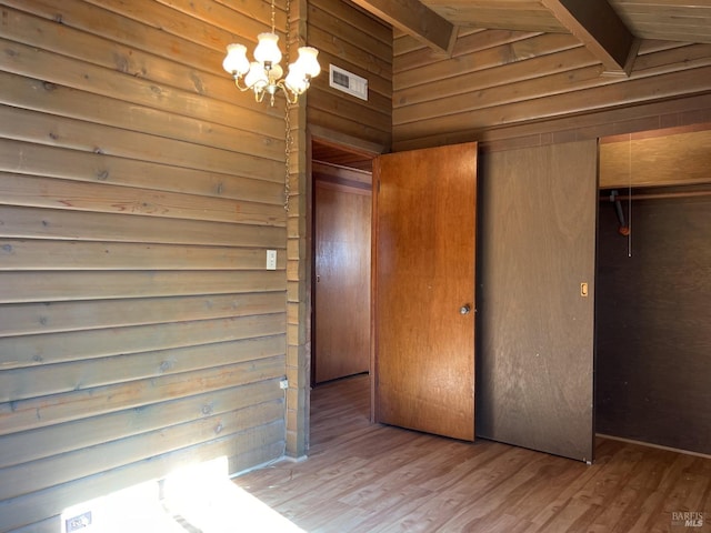 unfurnished bedroom featuring lofted ceiling with beams, wooden walls, an inviting chandelier, and wood-type flooring