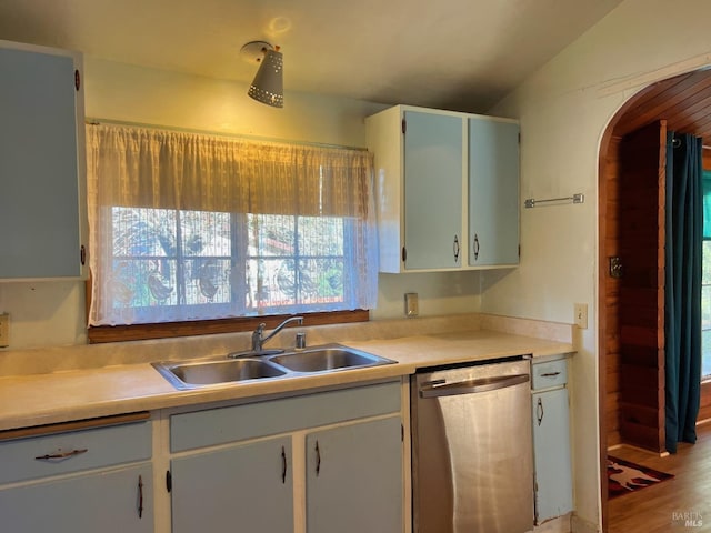 kitchen with arched walkways, lofted ceiling, light countertops, stainless steel dishwasher, and a sink