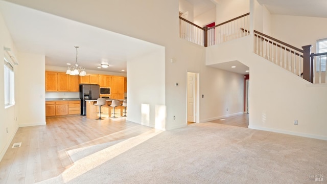 living area featuring a chandelier, light carpet, baseboards, light wood-style floors, and stairway