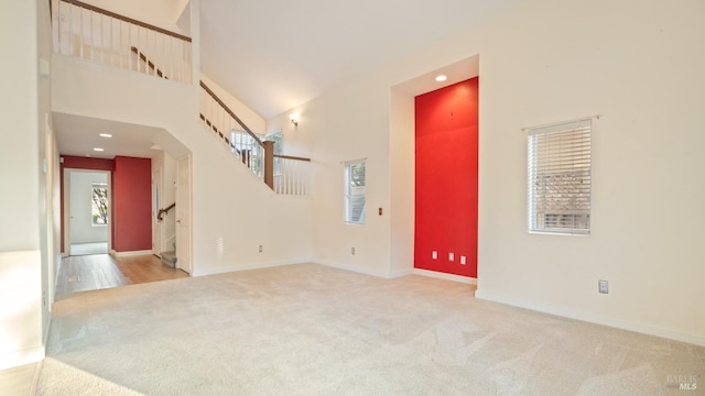 carpeted empty room with stairs, a high ceiling, recessed lighting, and baseboards