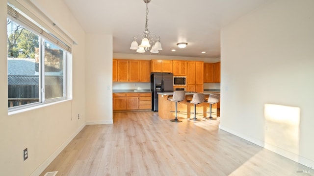 kitchen featuring a notable chandelier, a breakfast bar area, stainless steel microwave, black fridge with ice dispenser, and light wood-style floors