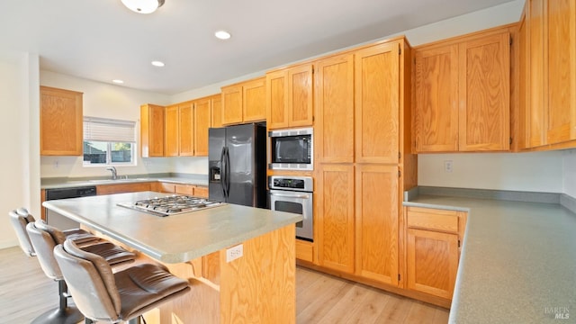 kitchen with stainless steel appliances, light countertops, a sink, a kitchen island, and a kitchen bar