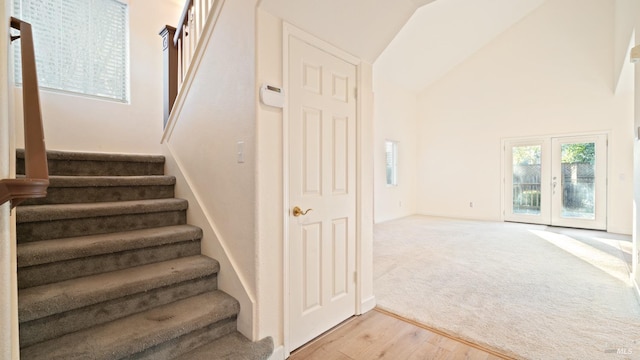 staircase featuring high vaulted ceiling, french doors, carpet flooring, and wood finished floors