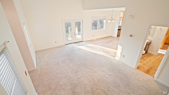 carpeted spare room featuring a chandelier, a towering ceiling, and baseboards