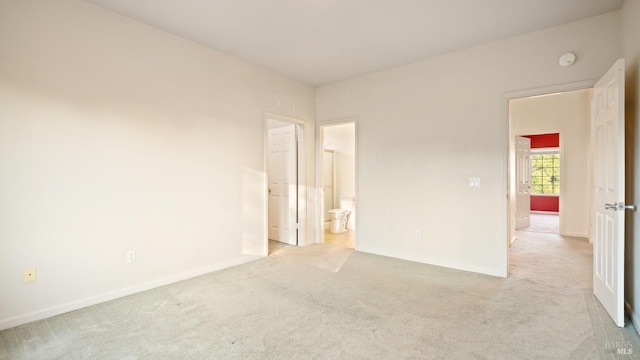 unfurnished bedroom with baseboards, ensuite bathroom, and light colored carpet