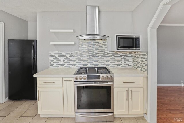 kitchen featuring stainless steel appliances, light tile patterned floors, wall chimney exhaust hood, and backsplash