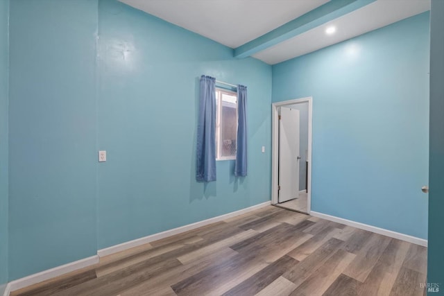 spare room featuring beamed ceiling and wood-type flooring