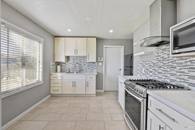 kitchen with light tile patterned floors, decorative backsplash, wall chimney range hood, sink, and stainless steel appliances