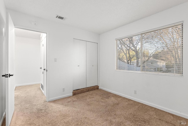 unfurnished bedroom with a closet, light colored carpet, and a textured ceiling