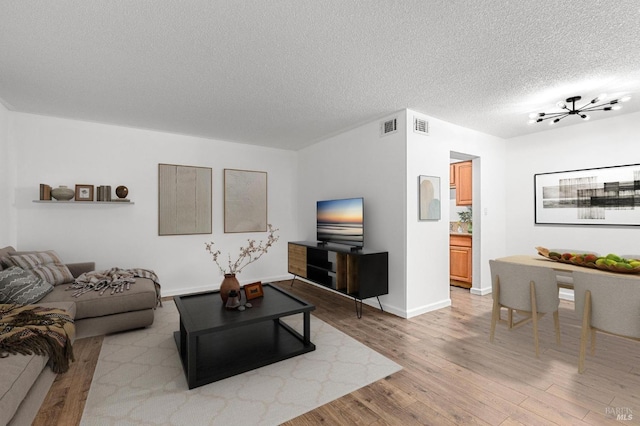 living room featuring a chandelier, light hardwood / wood-style floors, and a textured ceiling