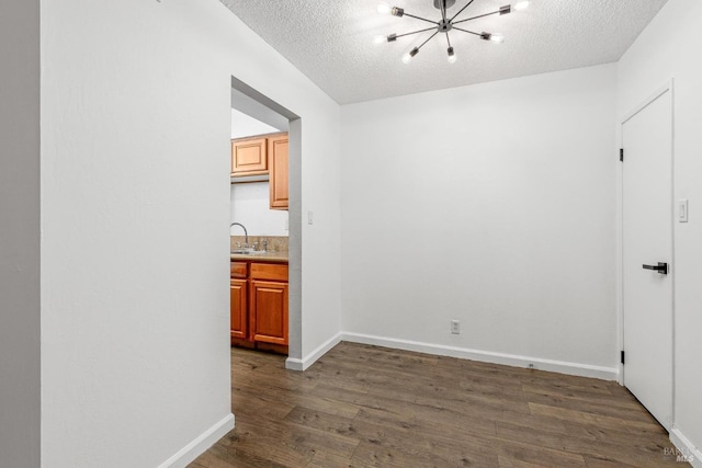 unfurnished room with sink, a textured ceiling, dark hardwood / wood-style floors, and an inviting chandelier