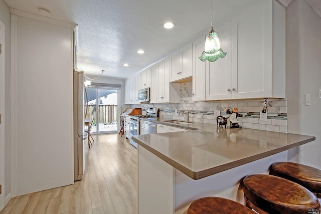 kitchen featuring a kitchen bar, white cabinets, sink, kitchen peninsula, and stainless steel appliances