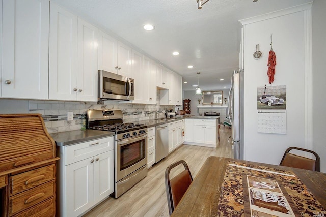 kitchen with white cabinets, light wood-type flooring, kitchen peninsula, pendant lighting, and stainless steel appliances