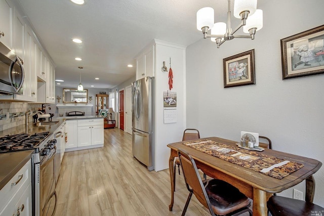 kitchen featuring appliances with stainless steel finishes, decorative light fixtures, white cabinetry, light hardwood / wood-style floors, and decorative backsplash