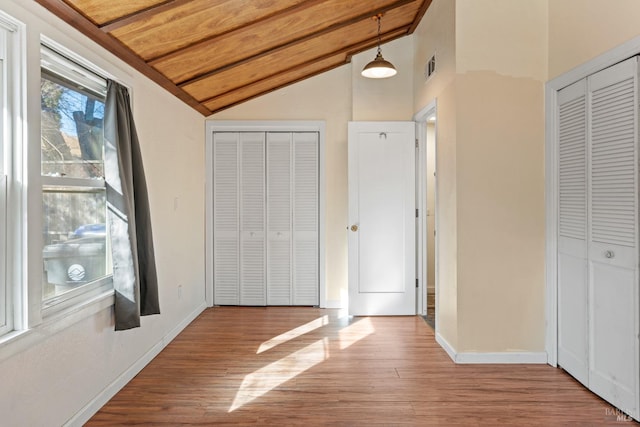 unfurnished bedroom with wood-type flooring, lofted ceiling, wood ceiling, and multiple closets