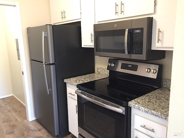 kitchen with light stone countertops, appliances with stainless steel finishes, white cabinets, and light wood-type flooring