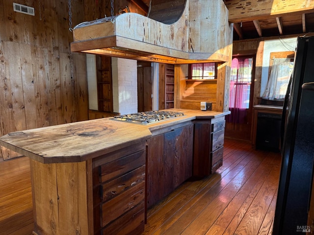 kitchen with black refrigerator, stainless steel gas stovetop, wooden counters, and wooden walls