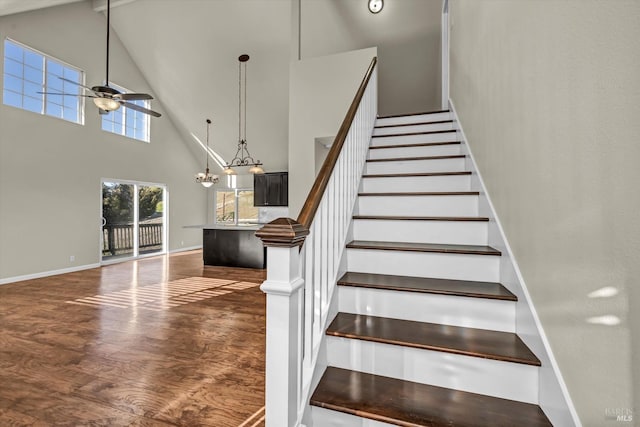 staircase featuring hardwood / wood-style flooring, ceiling fan with notable chandelier, and a high ceiling