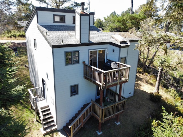 back of house with a chimney, roof with shingles, and stairs