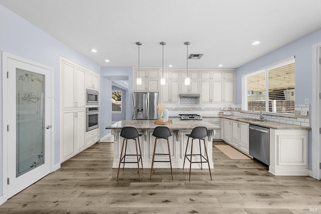 kitchen with a center island, appliances with stainless steel finishes, white cabinetry, sink, and decorative light fixtures