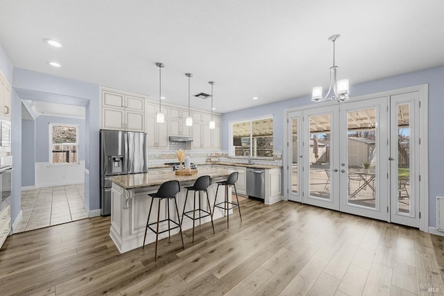 kitchen featuring a center island, decorative light fixtures, white cabinetry, stainless steel appliances, and a kitchen breakfast bar