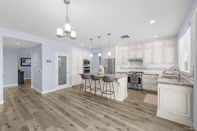 kitchen with pendant lighting, appliances with stainless steel finishes, a center island, tasteful backsplash, and sink