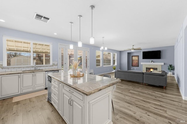 kitchen featuring pendant lighting, white cabinets, a center island, sink, and light stone counters