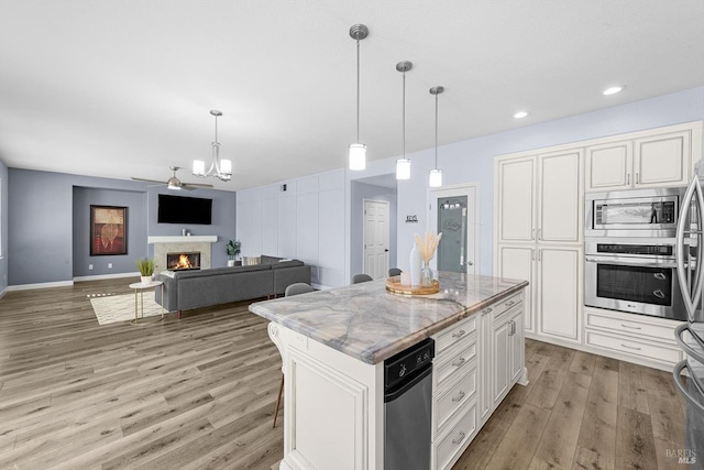 kitchen featuring a center island, light stone countertops, appliances with stainless steel finishes, white cabinets, and decorative light fixtures