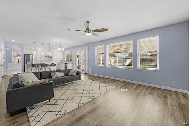 living room featuring ceiling fan with notable chandelier and light hardwood / wood-style flooring