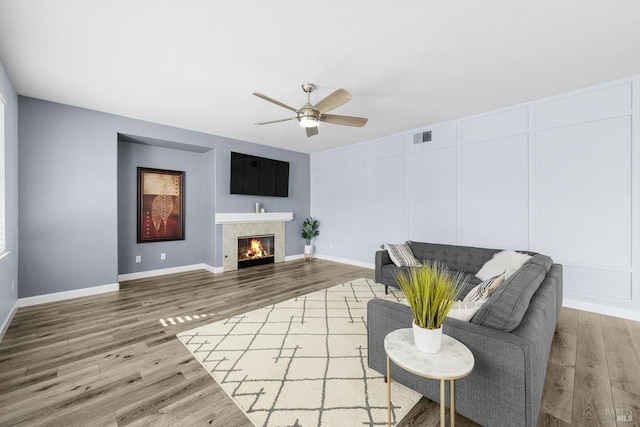 living room featuring hardwood / wood-style flooring, a tile fireplace, and ceiling fan