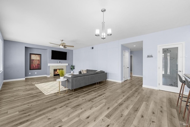 living room featuring ceiling fan with notable chandelier and light wood-type flooring