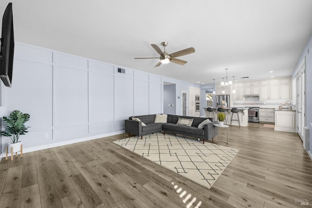 living room with sink, ceiling fan with notable chandelier, and light hardwood / wood-style flooring