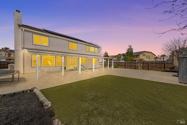 back house at dusk featuring a lawn, a trampoline, and a patio