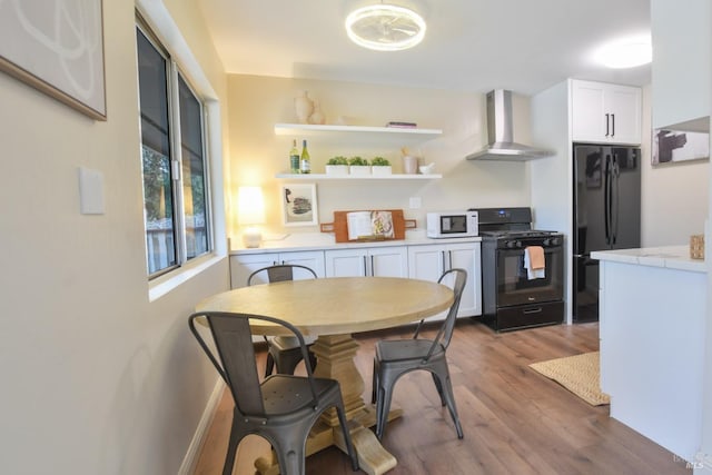 kitchen featuring hardwood / wood-style flooring, wall chimney range hood, white cabinets, and black appliances