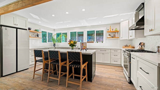 kitchen with exhaust hood, white cabinetry, a kitchen island, white refrigerator, and stainless steel range with gas cooktop