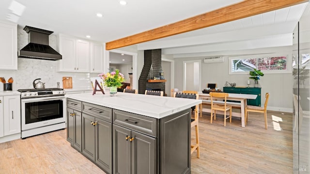 kitchen featuring beamed ceiling, white cabinetry, wall chimney range hood, a kitchen island, and stainless steel gas range oven