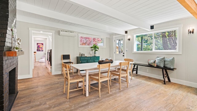 dining room featuring a wall mounted air conditioner, light hardwood / wood-style flooring, beamed ceiling, and a fireplace