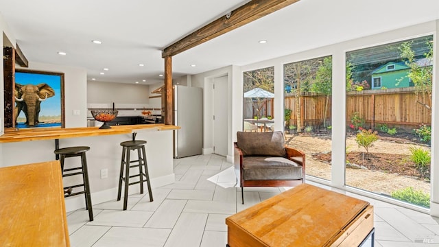 interior space with a kitchen bar, light tile patterned floors, stainless steel fridge, and beam ceiling