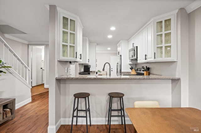 kitchen featuring appliances with stainless steel finishes, white cabinets, a kitchen breakfast bar, kitchen peninsula, and light stone countertops